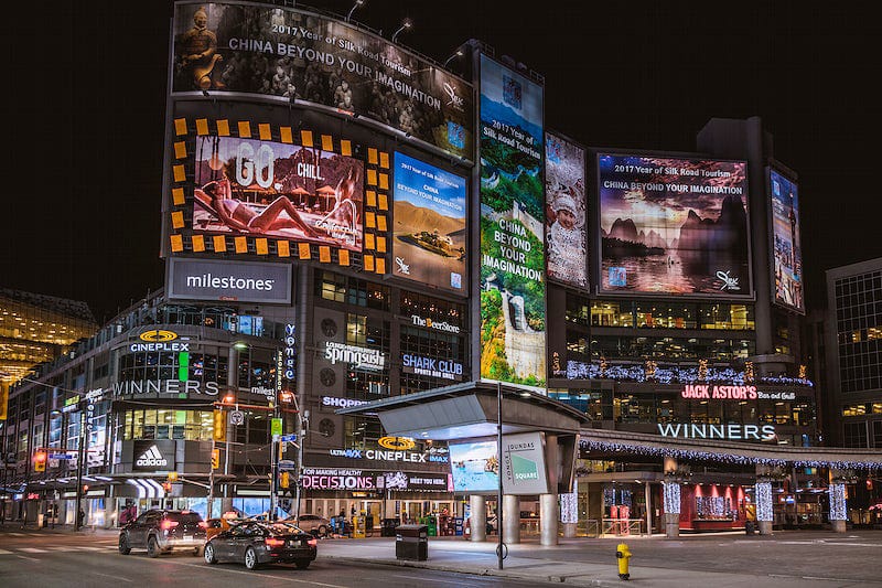 Neon advertising screens in a city square at night